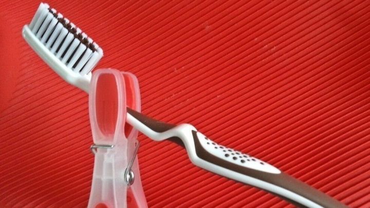 Eine Zahnb&uuml;rste ist an einer W&auml;scheklammer befestigt und steht vor einem roten Hintergrund, bereit zum Einsatz beim Reisen.