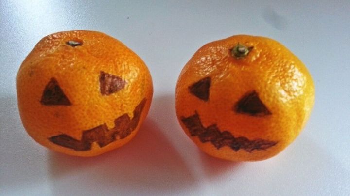 Zwei orangefarbene Mandarinen sind geschnitzt und sehen aus wie gruselige K&uuml;rbisse, perfekt f&uuml;r Halloween-Dekoration.