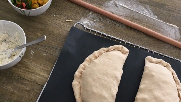 Zwei rohe Calzone-Teigst&uuml;cke liegen auf einer Arbeitsfl&auml;che, umgeben von frischem Gem&uuml;se und F&uuml;llungen f&uuml;r Pizza Calzone t&uuml;rkischer Style.