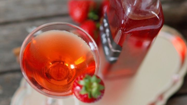 Ein Glas mit fruchtigem Lik&ouml;r steht auf einem Silbertablett, w&auml;hrend eine Flasche im Hintergrund und Erdbeeren dekorieren.