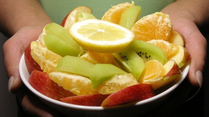Eine Sch&uuml;ssel mit buntem Obst, darunter &Auml;pfel, Melonen und Orangen, wird von H&auml;nden gehalten, die bereit sind, es zu genie&szlig;en.