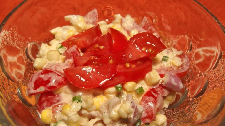 Frischer Tomaten-Maissalat wird appetitlich in einer Sch&uuml;ssel serviert, umgeben von buntem Gem&uuml;se und einer leichten Sauce.