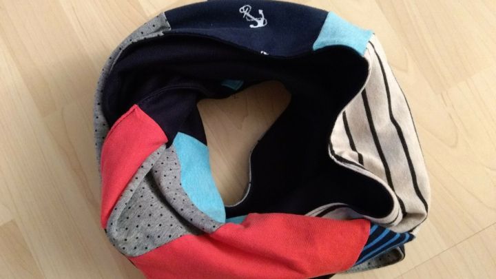 Ein bunter Loop-Schal, aus T-Shirt-Resten gefertigt, liegt ordentlich auf einem hellen Holztisch.