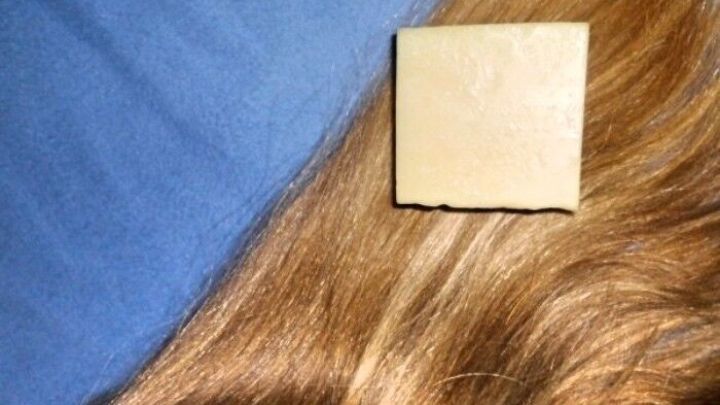 Ein festes St&uuml;ck Haarseife liegt auf einer gl&auml;nzenden Haarstr&auml;hne, umgeben von einem blauen Hintergrund.