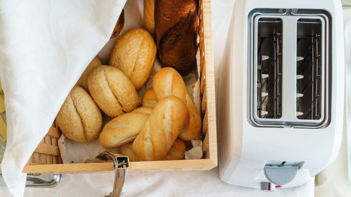 Goldene Br&ouml;tchen liegen in einer Holzkiste neben einem modernen Toaster, bereit zum Toasten in einer hellen K&uuml;chenszene.