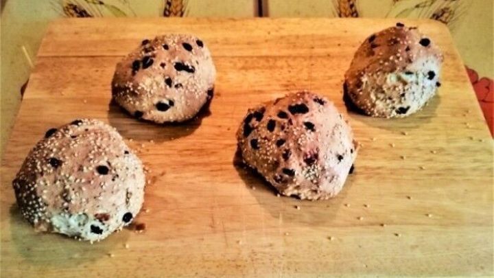 Farbenfrohe Br&ouml;tchen aus Hefeteig liegen frisch auf einem Holzbrett in einer warmen K&uuml;cheneinrichtung.