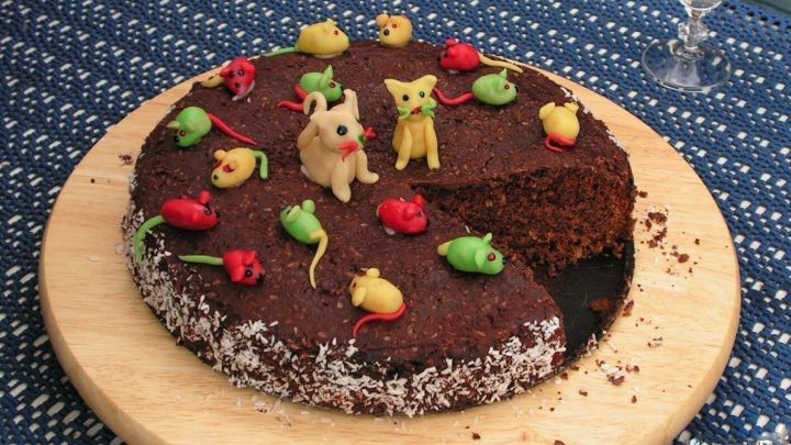 Ein runder Bumerang-Schokoladenkuchen mit bunten, dekorativen Figuren und einer Schnittstelle auf einem Holzbrett.