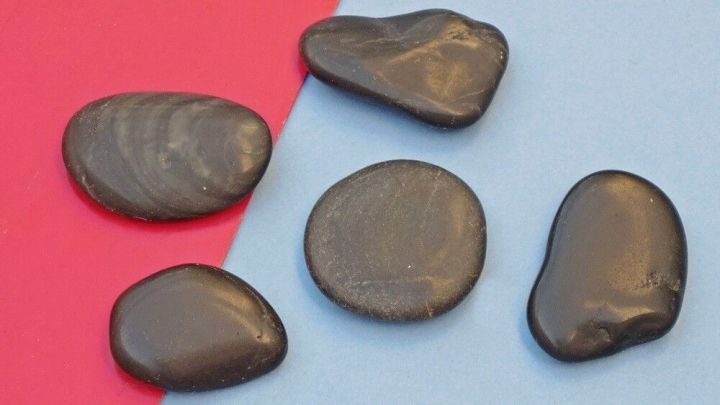 Schwarze Steine liegen auf einer blauen Unterlage, bereit f&uuml;r eine Gesichts-Massage gegen Falten.