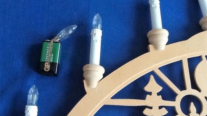 Defekte Birnchen liegen neben einem Holz-Lichterbogen auf einem blauen Untergrund; die Lichter sind zum Teil montiert.