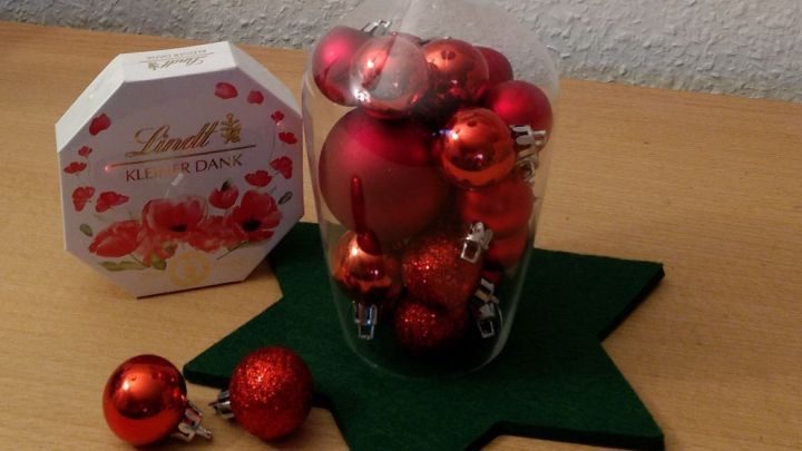 Ein Weinglas steht auf einem gr&uuml;nen Stern, gef&uuml;llt mit roten Weihnachtskugeln und einer Kerze dar&uuml;ber, festlich dekoriert.