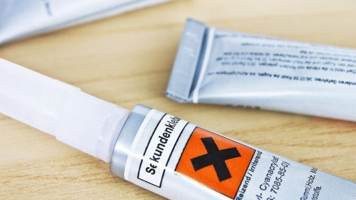 Ein Tuben-Kleber mit Warnhinweis liegt auf einem Holztisch, bereit zum Fixieren von Knoten oder Bastelprojekten.