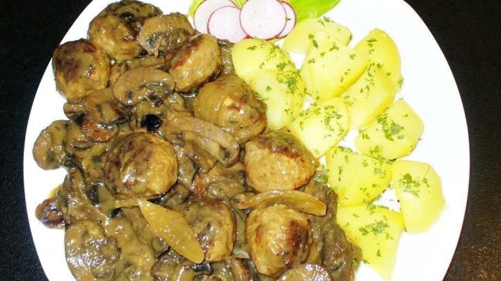 Saftige Hackb&auml;llchen mit frischen Champignons liegen auf einem Teller, umgeben von Petersilienkartoffeln und Salat.