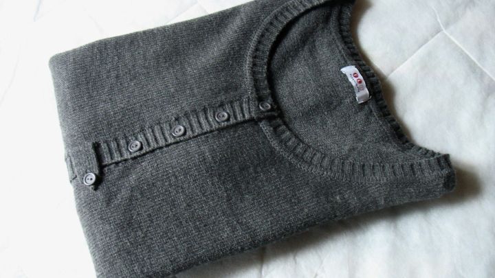 Ein ordentlich gefalteter grauer Pullover liegt auf einem hellen Untergrund, bereit zum Verstauen in einem Kleiderschrank.