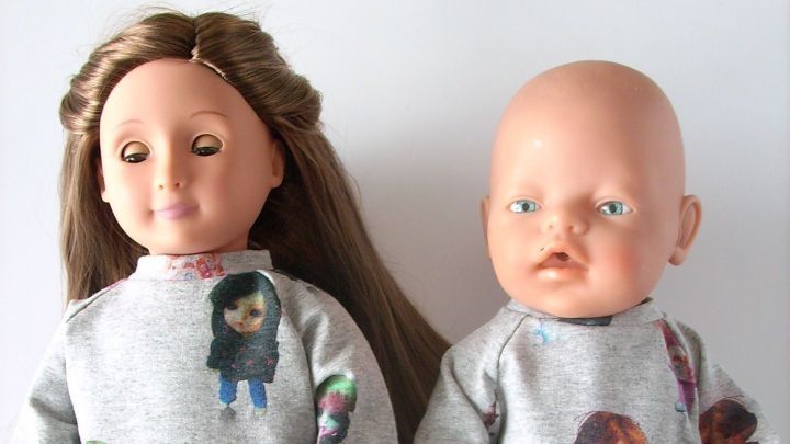 Zwei Puppen in bedruckter Kleidung stehen nebeneinander; eine tr&auml;gt rosa Blumenhose, die andere blaue Jeans.