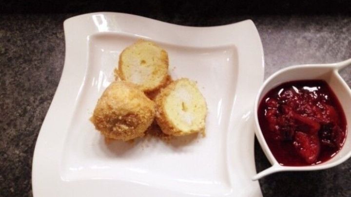 Drei goldene Quarkkn&ouml;del liegen auf einem eleganten Teller neben einer Portion Zwetschgenr&ouml;ster in einer wei&szlig;en Schale.