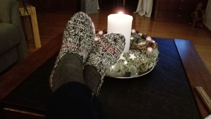 Gestrickte Haus- oder Bettsocken liegen entspannt auf einem Tisch neben einer brennenden Kerze in einer gem&uuml;tlichen Umgebung.