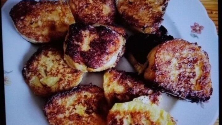 Auf einem wei&szlig;en Teller liegen braun gebratene Dampfnudeln, die appetitlich angerichtet sind, umgeben von einem Holzuntergrund.