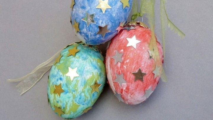 Bunte Ostereier mit Sternen liegen zusammen, dekoriert mit Schleifen, auf einem grauen Hintergrund.