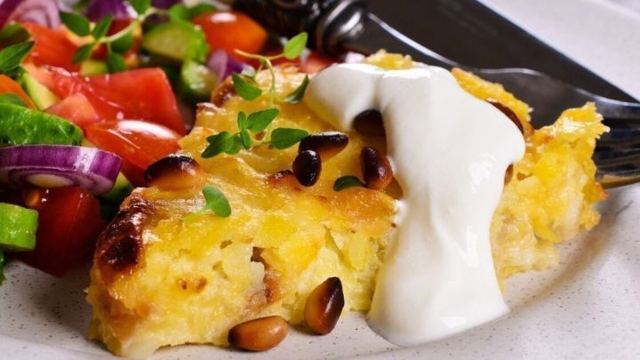 Ein Teller mit einer k&ouml;stlichen Kartoffelauflaufform und frischem Gem&uuml;se, umgeben von geschmackvollen Beilagen.