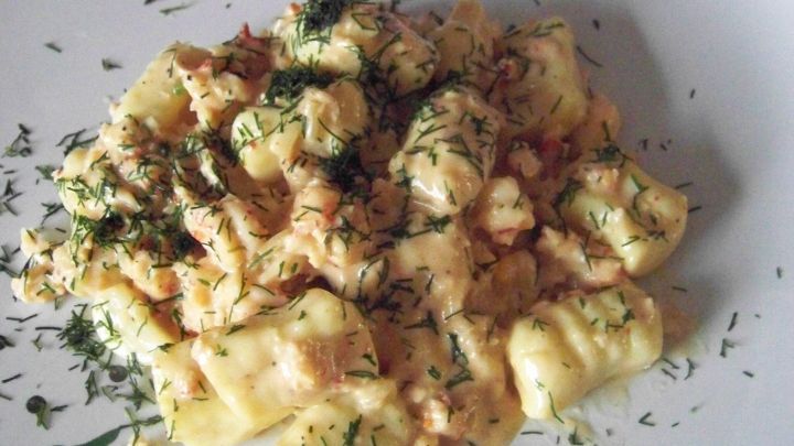 Gnocchi mit Krebsfleisch liegen auf einem wei&szlig;en Teller, umgeben von frischen Kr&auml;utern und einer cremigen, aromatischen Sauce.