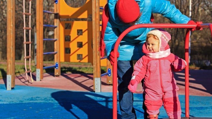 Ein Erwachsener hilft einem Kind auf einem Spielplatz, w&auml;hrend sie sich warm anziehen, um in der K&auml;lte zu spielen.