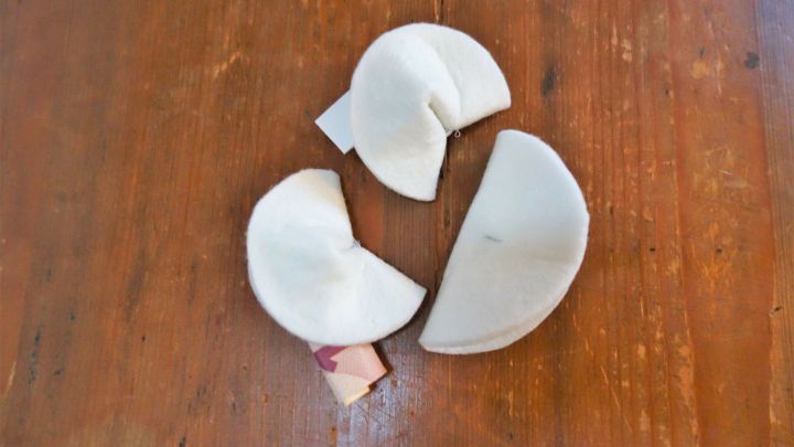 Drei Filz-Gl&uuml;ckskekse liegen auf einem Holztisch, gebrochen und bereit, ihre Botschaften zu offenbaren.