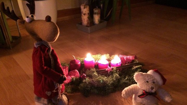 Ein Rentier und ein Teddyb&auml;r stehen neben einem Adventskranz mit brennenden Kerzen in einer gem&uuml;tlichen Wohnatmosph&auml;re.