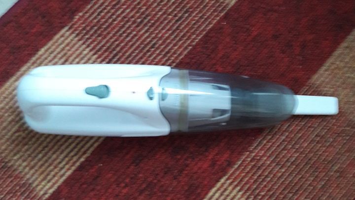 Ein wei&szlig;er Handstaubsauger liegt auf einem gestreiften Teppich und wartet auf die Reparatur im Caf&eacute;.