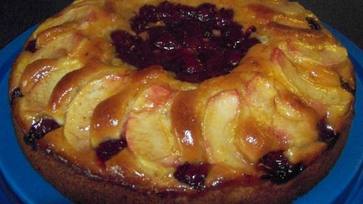 Ein saftiger Apfel-Kirsch-Kuchen liegt auf einem blauen Teller, umgeben von einer warmen K&uuml;chenatmosph&auml;re.