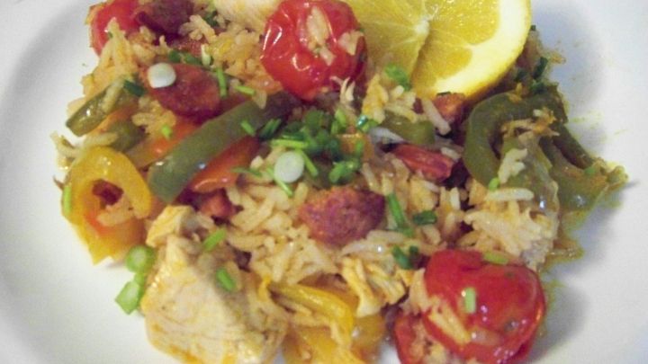 Bunte H&auml;hnchenpfanne mit Chorizo, Paprika, Tomaten und einem Zitronenschnitz, angerichtet auf einem wei&szlig;en Teller.