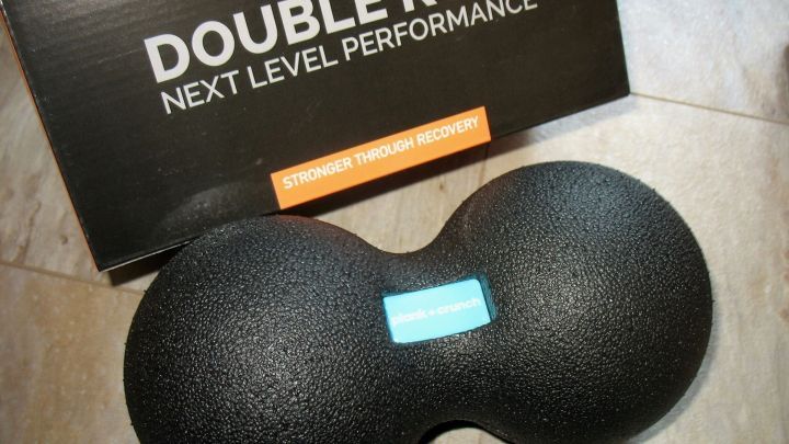 Ein schwarzer Faszienroller liegt auf einem hellen Boden, umgeben von einer Verpackung, um R&uuml;ckenschmerzen zu lindern.