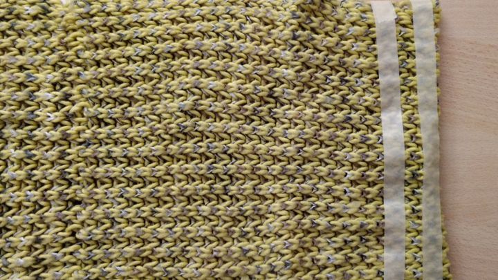 Ein gestrickter Loop liegt auf einem Tisch und zeigt eine gut erkennbare Struktur mit einem schlichten, gemusterten Design.