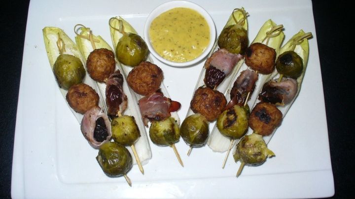 Spie&szlig;e mit Hackb&auml;llchen und Rosenkohl sind auf einem wei&szlig;en Teller angerichtet, umgeben von einer k&ouml;stlichen Dip-Sauce.