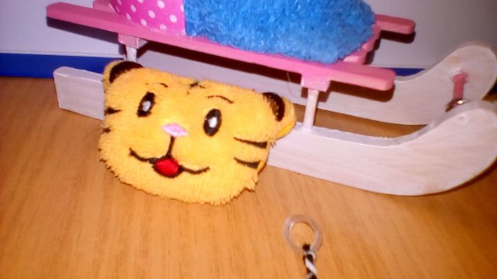 Ein gelbes Puppenkissen in Form eines Tigers liegt unter einem kleinen Schlitten mit bunten Decken.