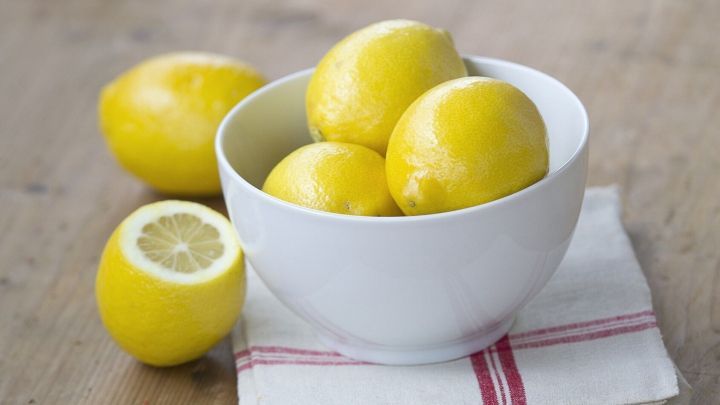 Eine wei&szlig;e Sch&uuml;ssel mit gelben Zitronen auf einem Holzarbeitsplatz, umgeben von einem Geschirrtuch.