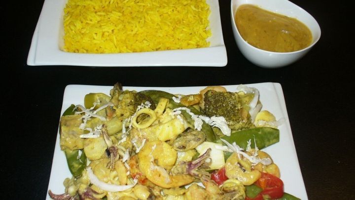 Leckeres Meeresfr&uuml;chte-Curry liegt auf einem Teller, begleitet von Kurkumareis und einer w&uuml;rzigen Sauce in einer Sch&uuml;ssel.