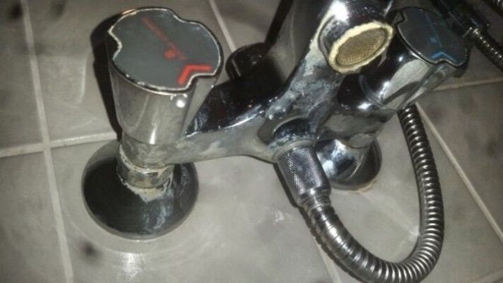 Ein verchromter Wasserhahn mit hartn&auml;ckigen Kalkflecken, der auf einer Fliese in einem Badezimmer montiert ist.