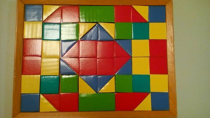 Bunte Kartonteile sind in einem Holzrahmen angeordnet, die ein farbenfrohes Legespiel-Muster bilden.