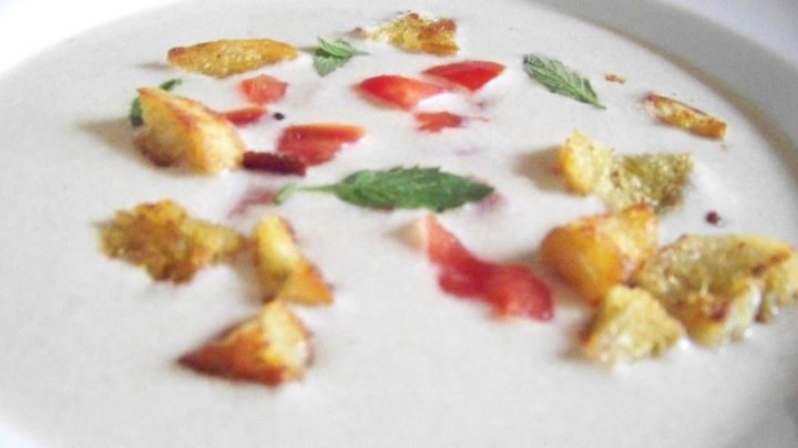 Eine cremige Auberginen-Suppe wird in einer wei&szlig;en Sch&uuml;ssel pr&auml;sentiert, dekoriert mit knusprigen Brotw&uuml;rfeln und frischen Kr&auml;utern.