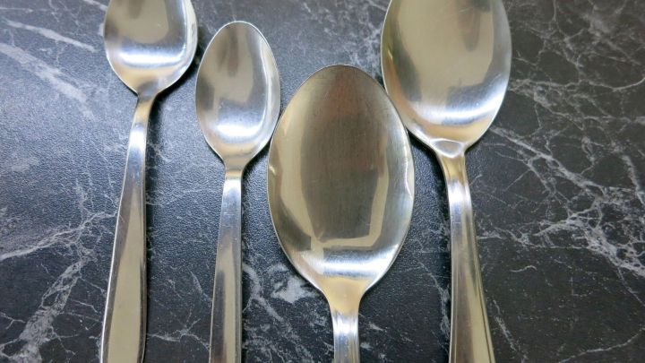 Vier gl&auml;nzende Silberl&ouml;ffel liegen auf einer dunklen Marmoroberfl&auml;che, bereit zur Pflege gegen Rost mit Melkfett.