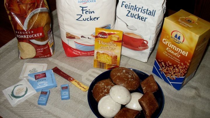 Zwei T&uuml;ten Zucker und weitere Zutaten liegen auf einem Tisch, w&auml;hrend Eier und Snacks in einer Sch&uuml;ssel arrangiert sind.