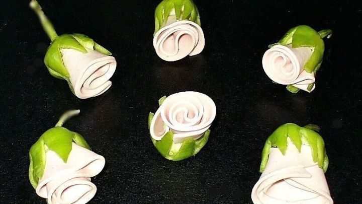 Dekorative R&ouml;schen aus Wurst sind kunstvoll geformt und auf einem dunklen Tisch arrangiert, ideal f&uuml;r ein Buffet.