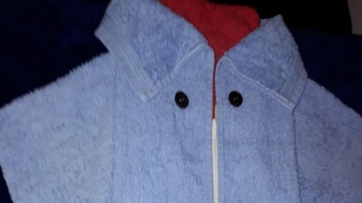 Ein flauschiges, hellblaues Handtuch mit einem roten Kragen liegt ordentlich gebunden auf einem dunklen Hintergrund.