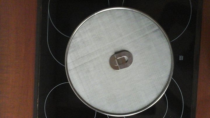 Ein runder Spritzschutz liegt auf einem Topf auf einer Kochplatte, um Fettspritzer beim Kochen zu vermeiden.