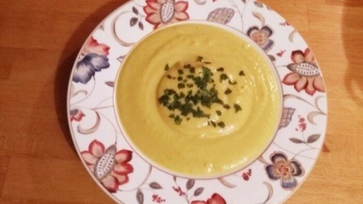 Eine cremige Blumenkohlsuppe mit K&auml;se und Kurkuma, serviert in einer bunten, floral dekorierten Sch&uuml;ssel auf einem Holztisch.