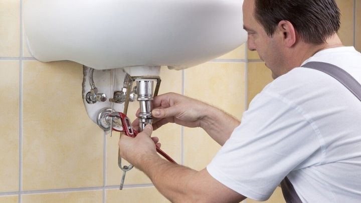 Ein Handwerker arbeitet an einer Abwasserleitung unter einem Waschbecken, um eine Verstopfung zu beseitigen.