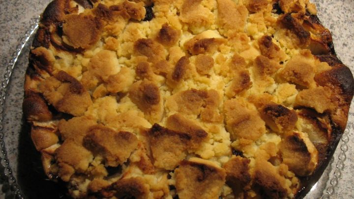 Eine goldene Apfeltorte mit Butterstreuseln liegt auf einem silbernen Teller und hat eine knusprige Oberfl&auml;che.