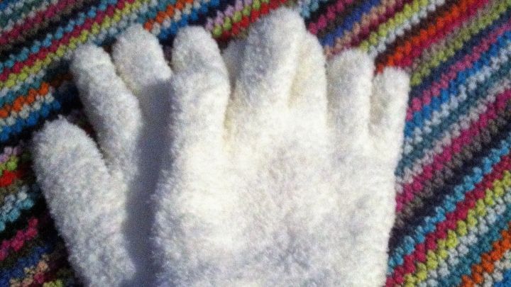 Wei&szlig;e Synthetik-Pl&uuml;sch-Handschuhe liegen auf einem bunten, gestreiften Tuch und sind bereit zum Staubwischen.