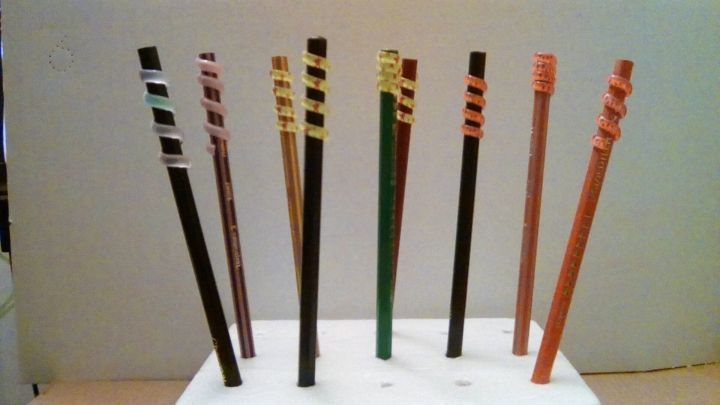 Bunte Stifte stehen aufrecht in einer Halterung. Schmuckaufs&auml;tze zieren die Spitzen und verleihen ihnen einen kreativen Look.