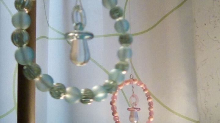 Ein bunter Anh&auml;nger aus Perlen h&auml;ngt an einer Lampe, umgeben von einer hellen Wand mit grafischem Muster.